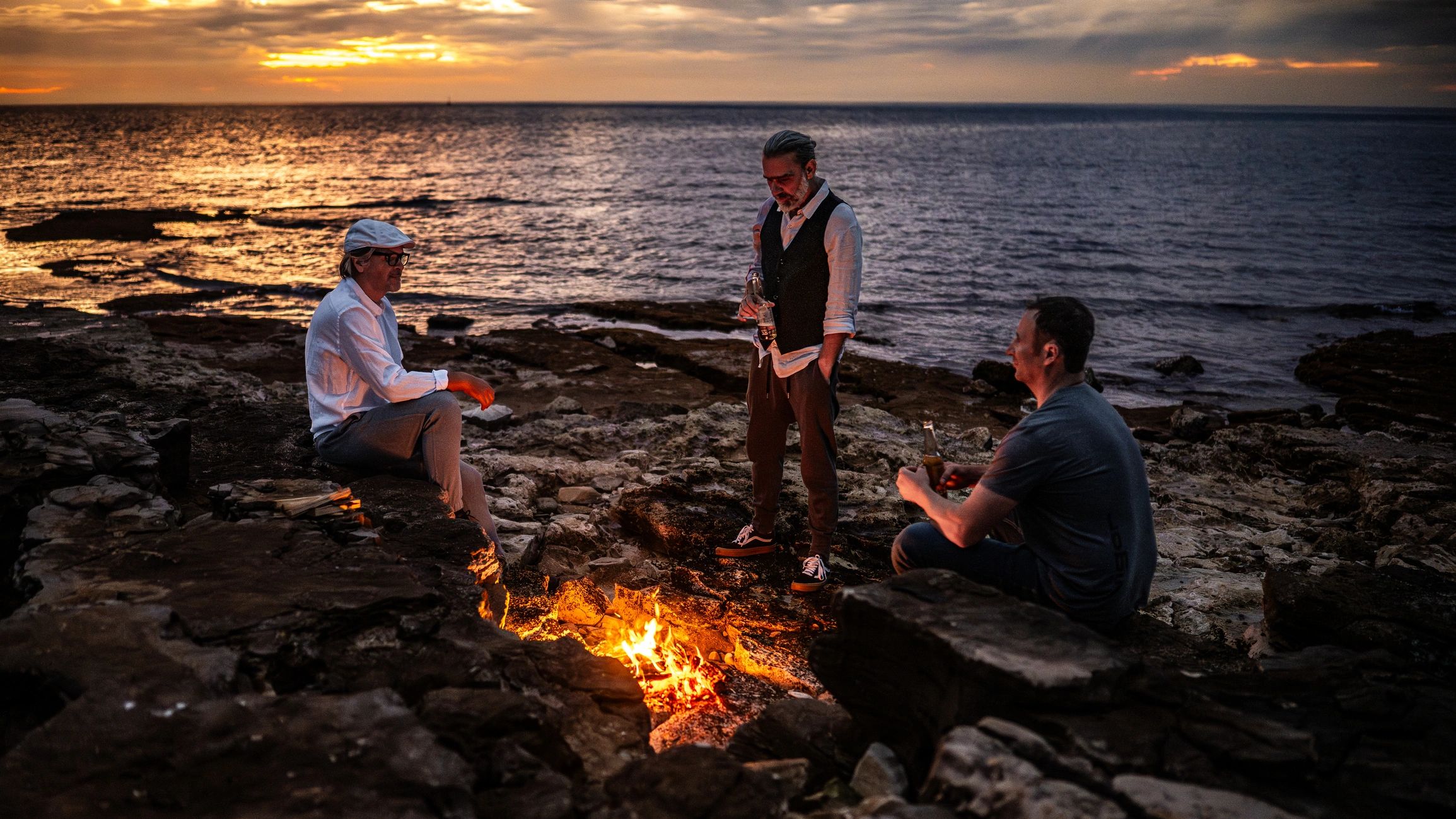 Three men connecting around a campfire at sunset